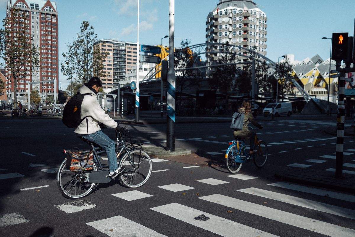 Bicicliști traversând, cu turnul Blaak și casele cubice în spate