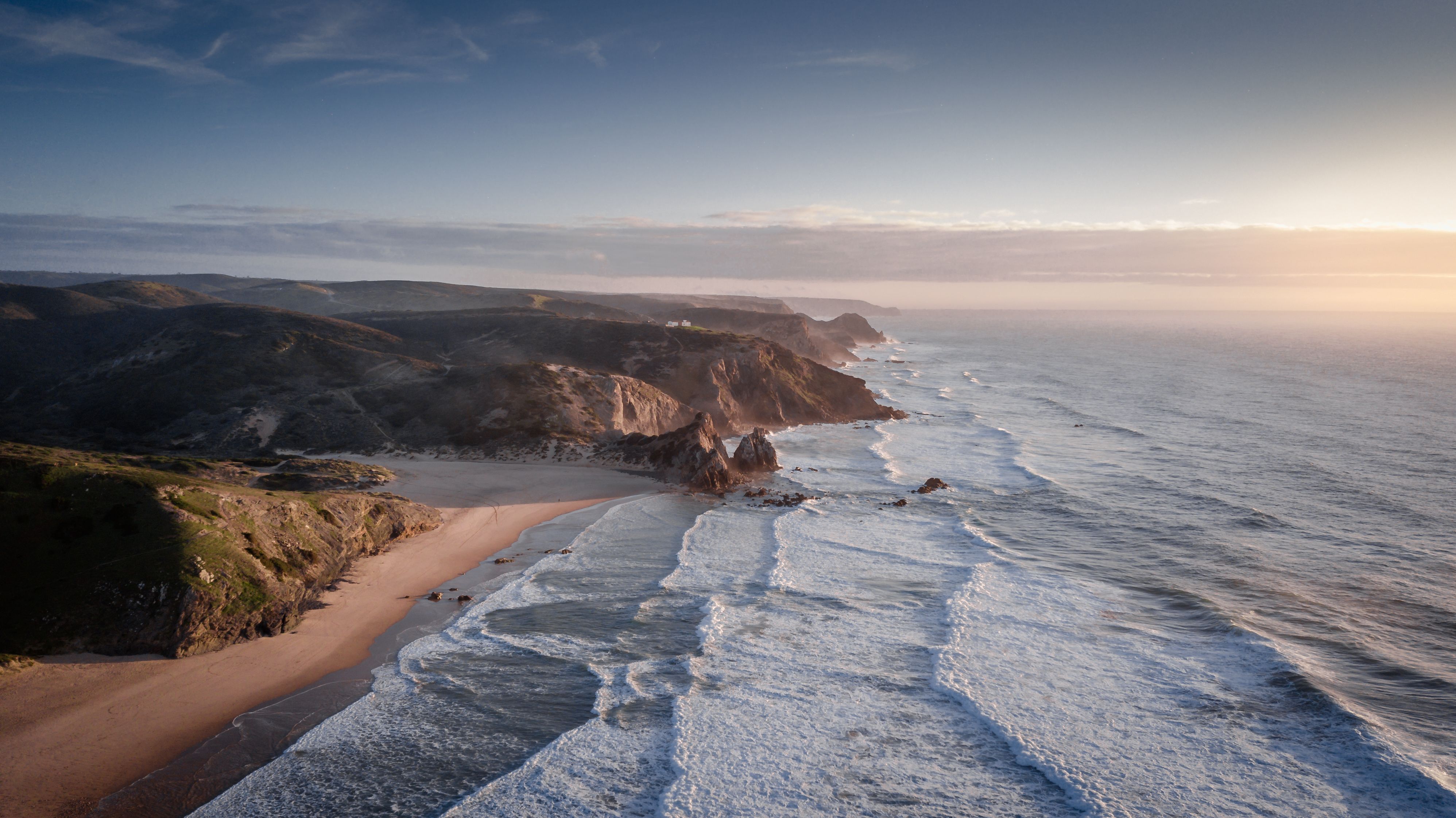 A breathtaking aerial view of the rugged coastline near Aljezur, Portugal at sunrise.