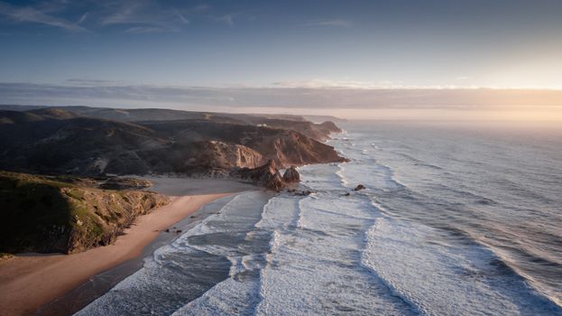 A breathtaking aerial view of the rugged coastline near Aljezur, Portugal at sunrise.
