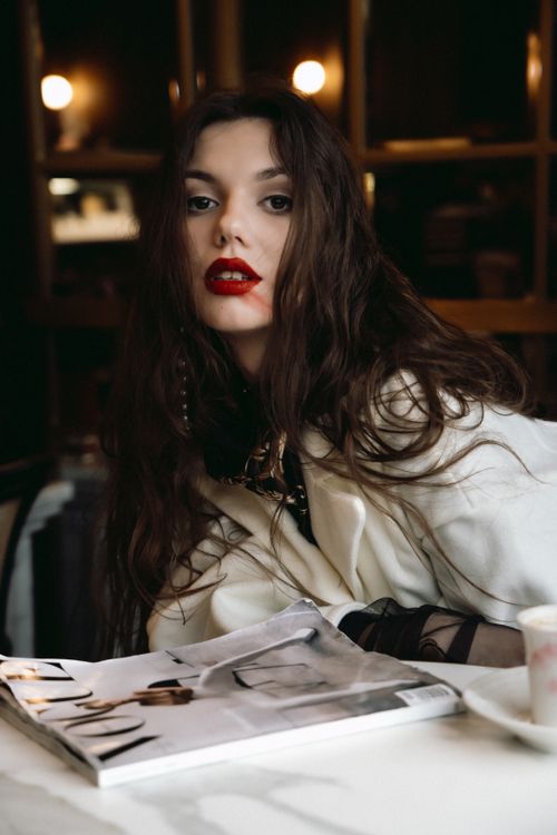Free A fashionable young woman with red lips poses artistically in a cozy cafe setting. Stock Photo