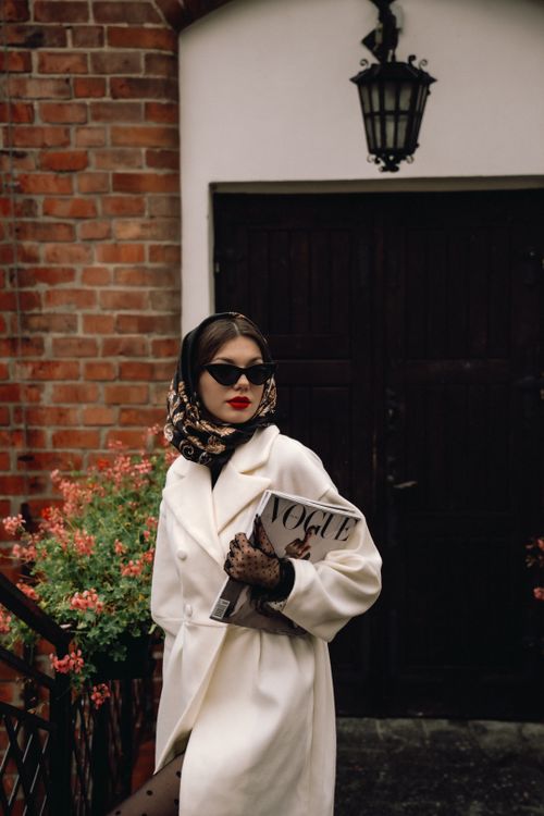 Free Stylish woman in a coat with headscarf holding a fashion magazine, exuding classic glamour. Stock Photo