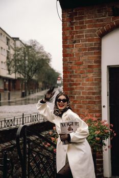 Elegantly dressed woman with a magazine posing cheerfully outside on a rainy day.