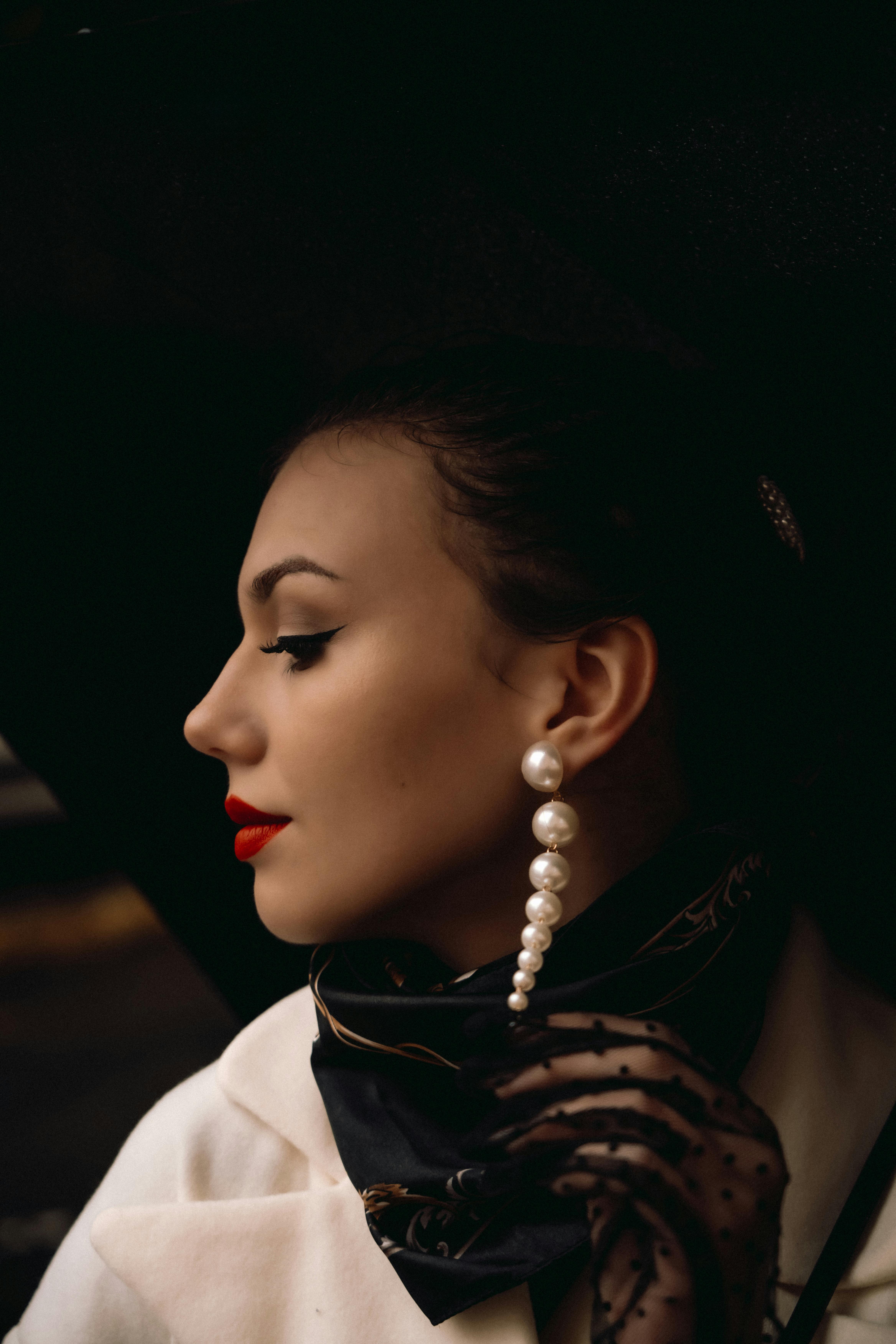 side profile of a young elegant woman with red lips and wearing pearl earrings