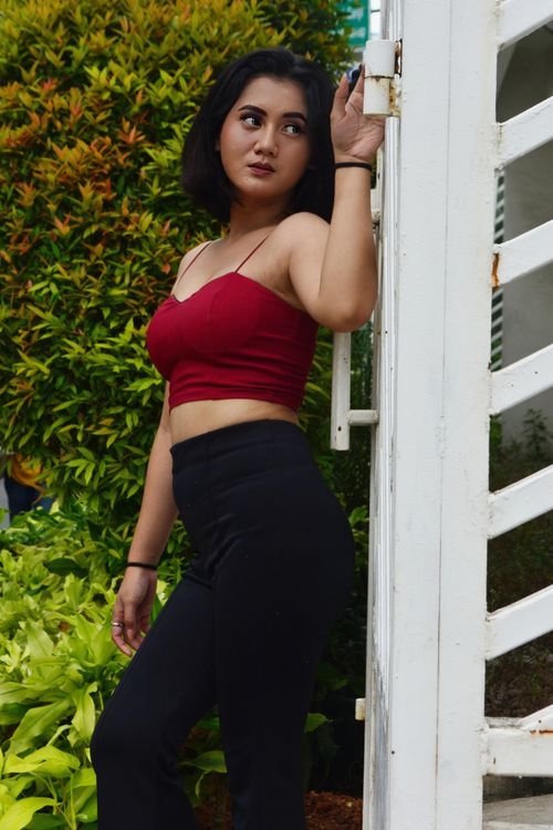 Free Fashionable woman in a red top and black pants poses stylishly outdoors in Jakarta, Indonesia. Stock Photo