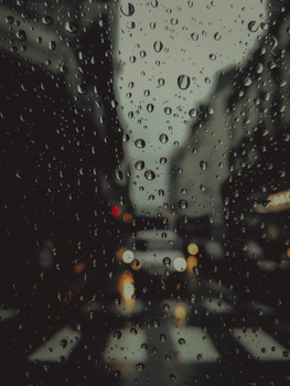 Blurred city street view through a window covered in rain droplets creating a moody ambiance.
