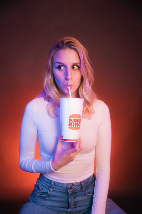 Free Woman in white blouse sipping from a Burger King cup in a creative studio shoot. Stock Photo