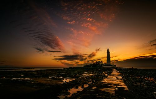 Free Dramatic sunset view of a lighthouse casting a silhouette over the ocean. Stock Photo