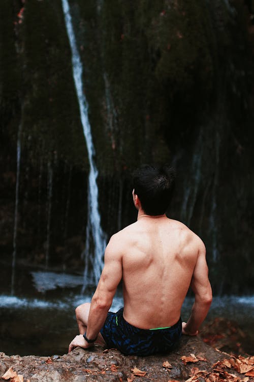Bare Back of a Man Sitting by a Waterfall