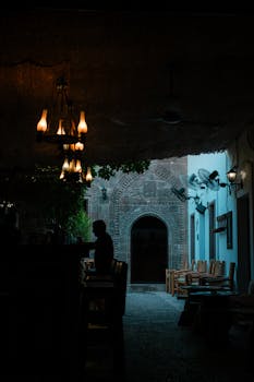 Silhouetted figure in a cozy courtyard at dusk, featuring ornate doors and warm lighting.