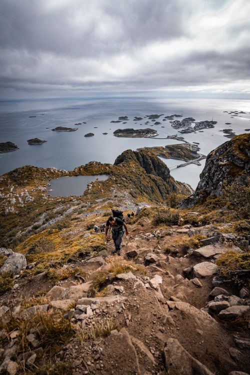 Free Adventurer hiking on rocky trail overlooking stunning Lofoten Island seascape, Nordland, Norway. Stock Photo