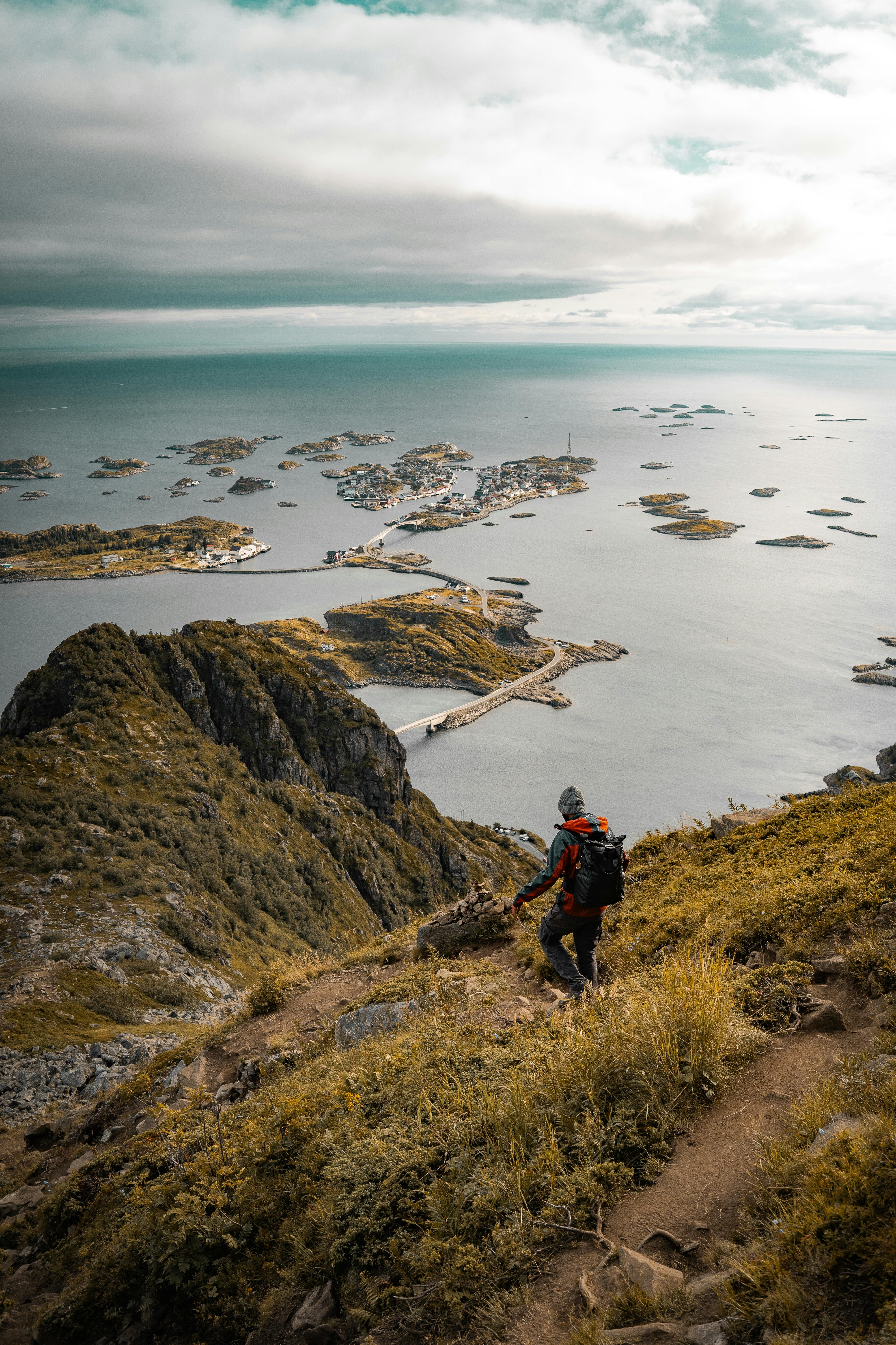 A hiker on a mountain path with a stunning view of Henningsvær islands in Norway's Nordland county.