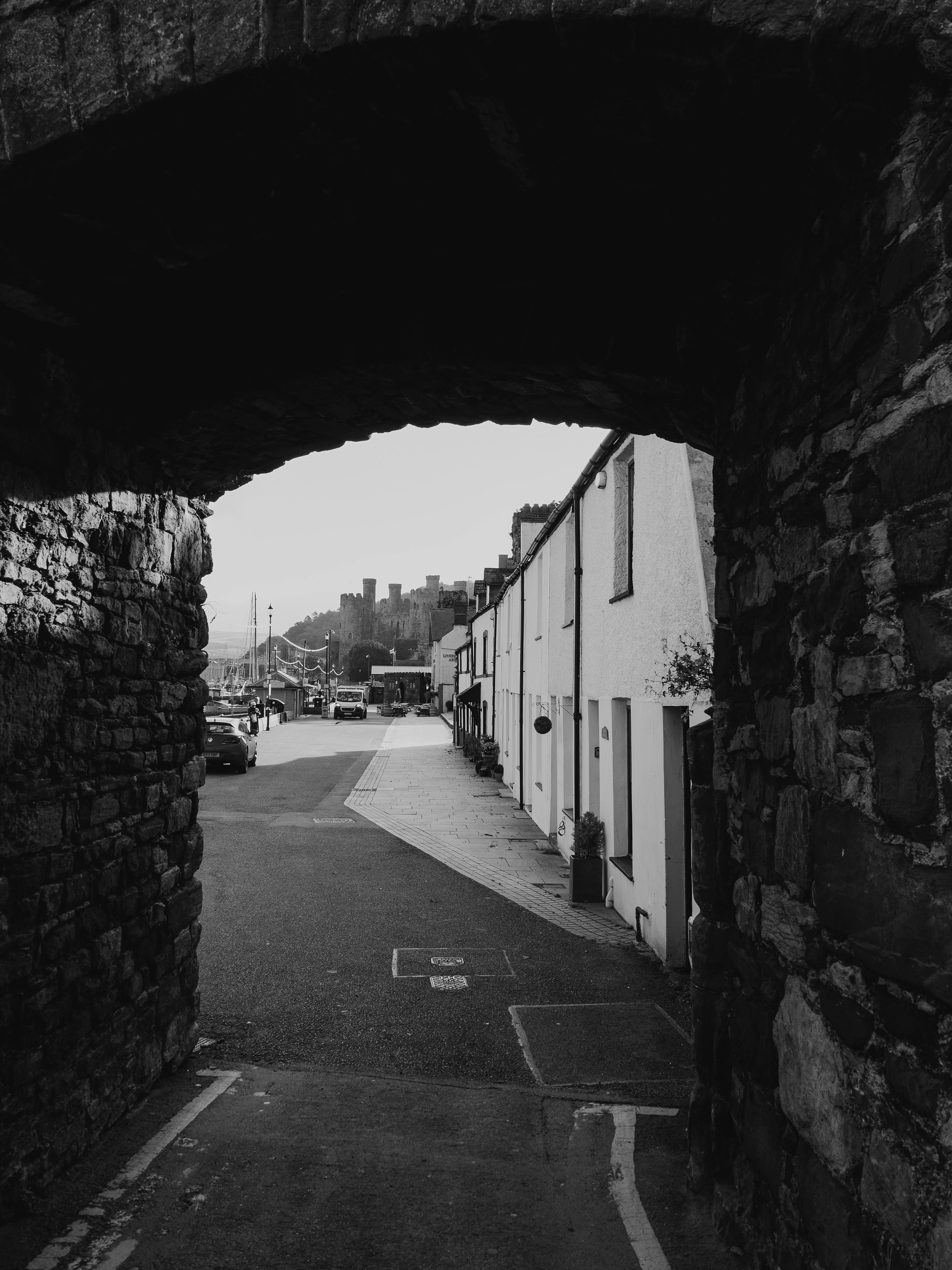 Black and white photo of a historic archway framing a city street in Conwy, Wales.