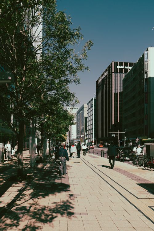 Free A sunlit street in Nagoya, Japan, bustling with people walking and surrounded by modern buildings. Stock Photo