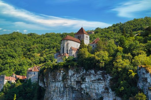 Picturesque medieval church nestled on a forested cliff with a vibrant sky.