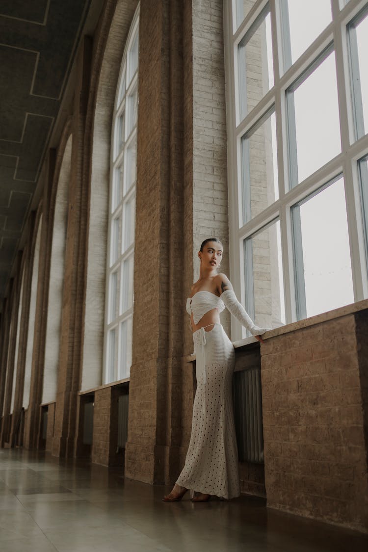 Young Woman In A White Top And Skirt Leaning Against A Wall 