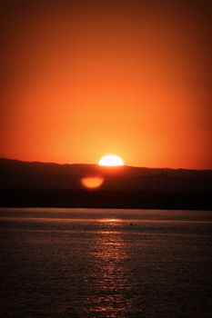 Golden sun setting over calm ocean, reflecting warm tones on water surface.