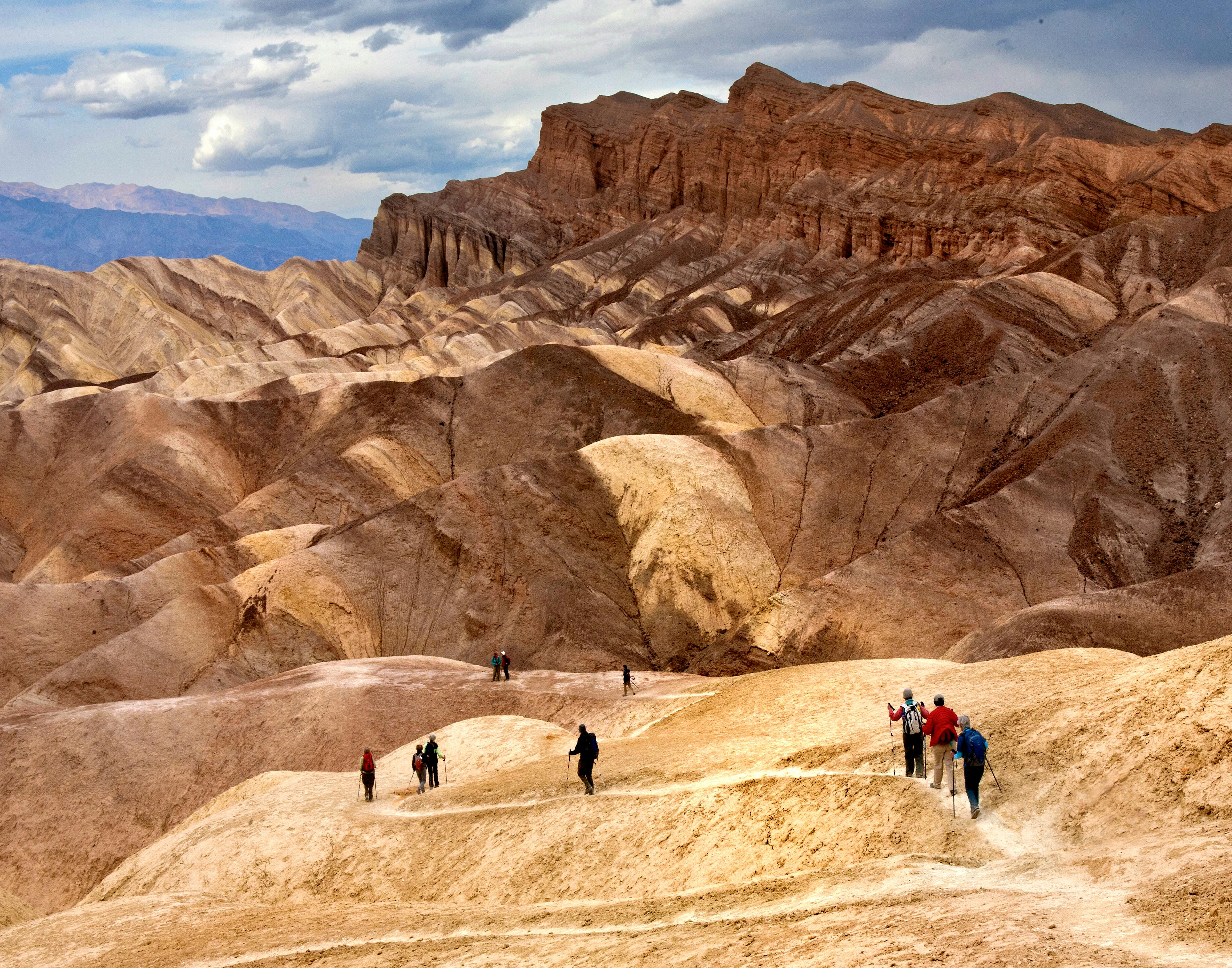 Group hiking through stunning desert dunes under cloudy skies.