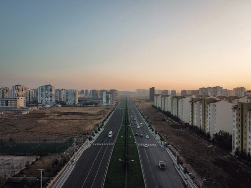Free Drone capture of a wide city avenue surrounded by buildings against a sunset sky. Stock Photo