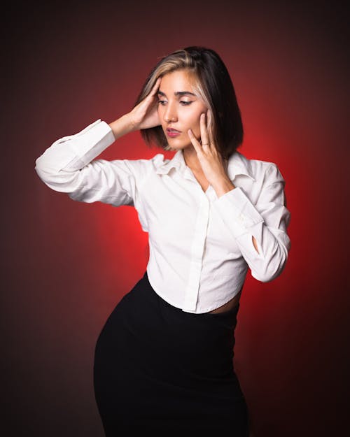 Free A woman in a white shirt and black skirt is holding her head Stock Photo