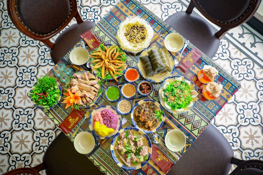 Overhead shared feast with fresh herbs, fried rolls, dipping sauces and bowls on patterned cloth