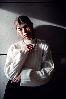 Portrait of a woman in a white sweater against a textured wall, dramatic lighting.