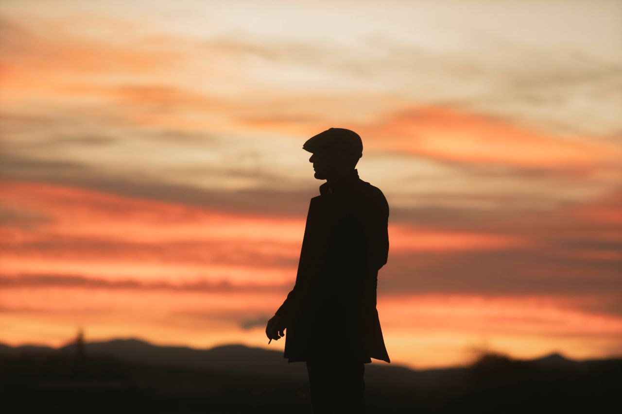 a silhouetted man in a hat stands against a dramatic sunset sky creati