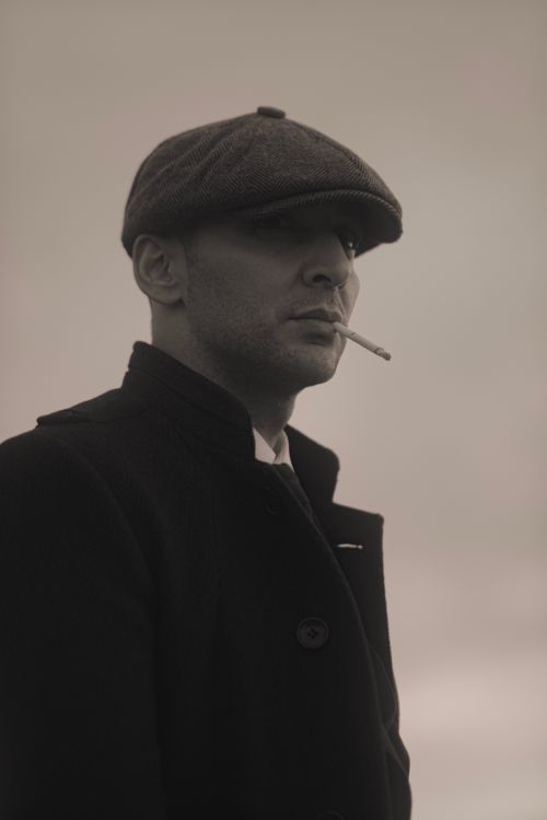 Free A striking vintage-style monochrome portrait of a man wearing a hat and smoking a cigarette. Stock Photo