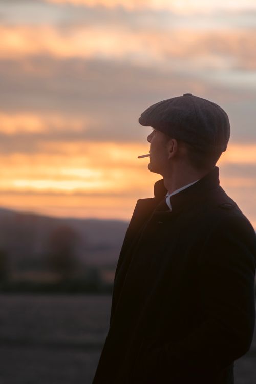 Free A man in vintage attire smoking a cigarette outdoors, gazing at a sunset. Stock Photo