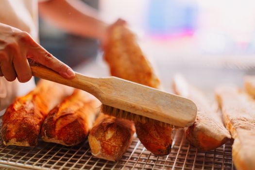 Freshly baked baguettes being brushed in a bakery setting. Perfect for food and artisan crafts imagery.