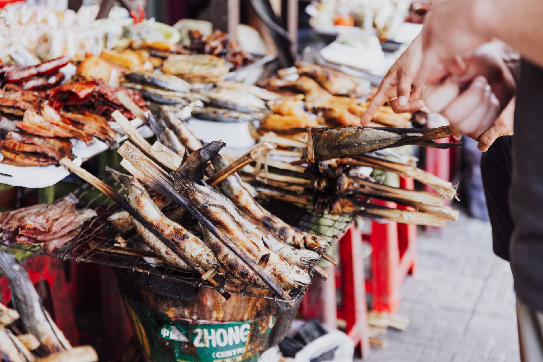 Explore the vibrant display of grilled fish and meats at a bustling street market stall.