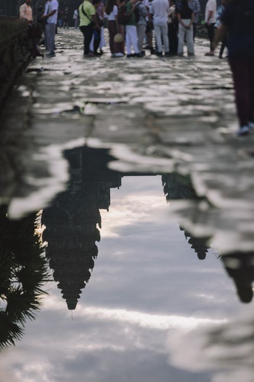 Free Reflection of Angkor Wat temple in a puddle on a cobbled pathway with tourists in the background. Stock Photo