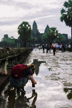A tourist with a red backpack photographs a reflection at Angkor Wat, Cambodia
