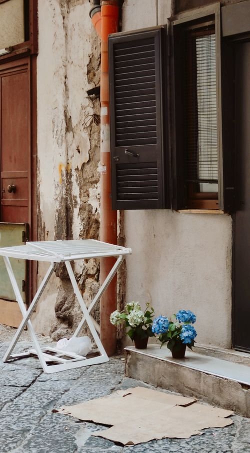 Free A rustic Naples street corner featuring a white table and potted hydrangeas, perfect for urban exploration. Stock Photo