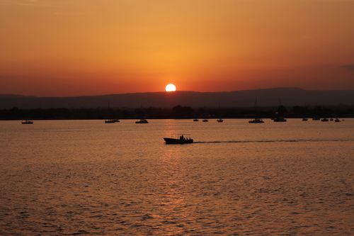 Free A tranquil scene of boats silhouetted against a vibrant sunset in Syracuse, Sicily. Stock Photo