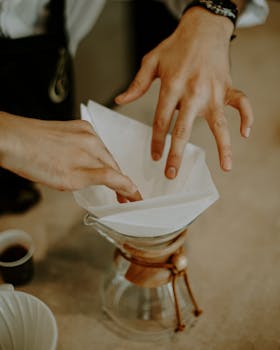 Close-up of a barista setting up a pour-over coffee maker with a filter, showing precise hand movements.