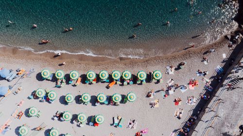 Free Drone shot of Amalfi beach showcasing sunbathers and umbrellas lining the shore. Stock Photo