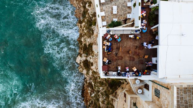 Stunning aerial shot of a seaside restaurant terrace in Polignano a Mare, Italy, overlooking the vibrant sea.