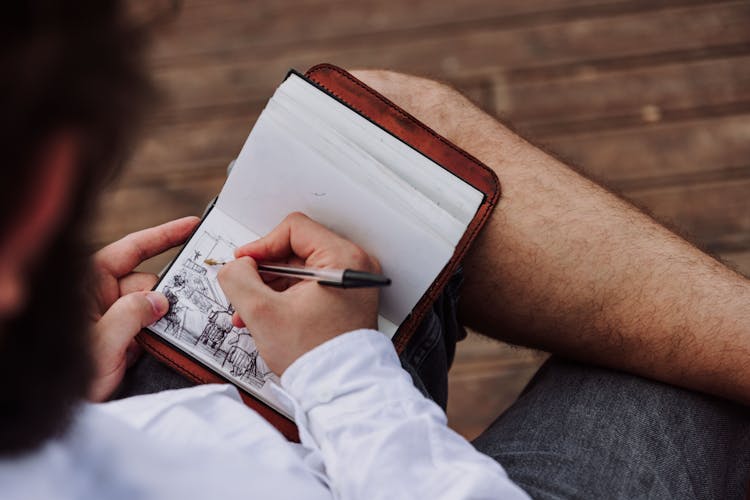 Man Sitting And Drawing In Notebook