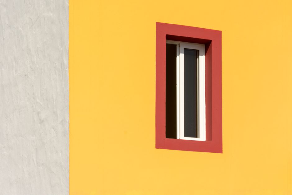 Geometric composition of a building's yellow facade with a red-framed window.