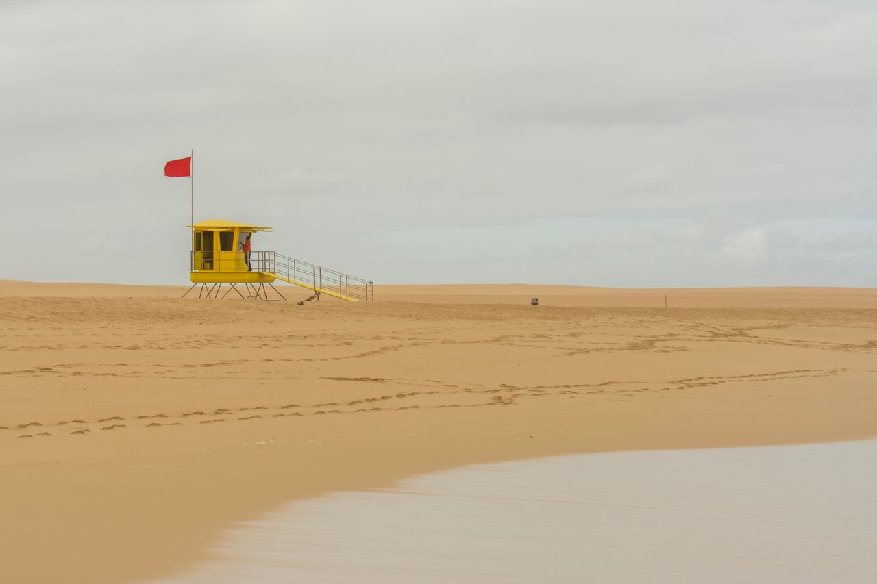 a yellow lifeguard tower with a red flag on a deserted sandy beach und