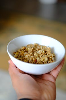 Close-up of a hand holding a bowl of healthy granola, perfect for a nutritious breakfast.