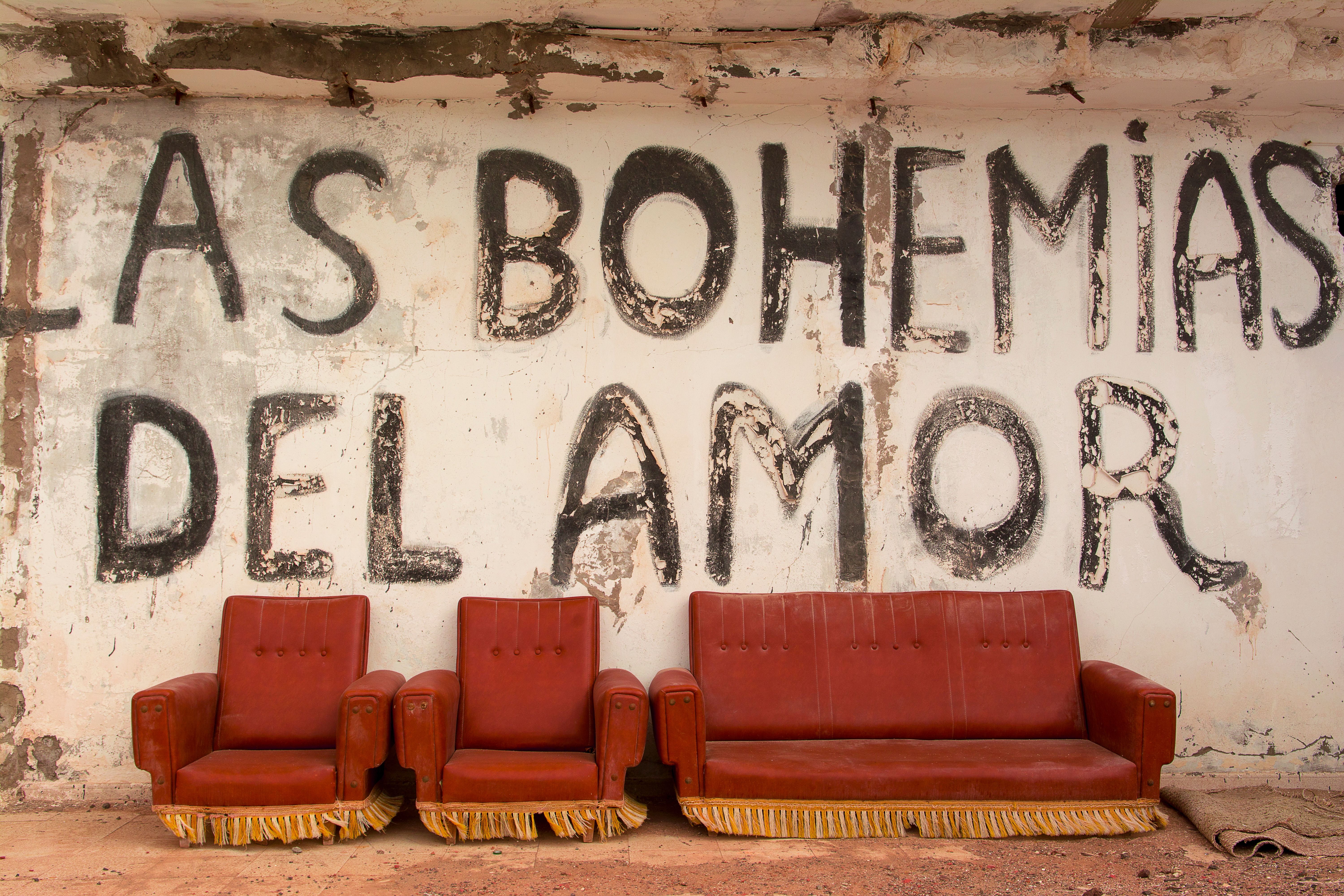 Red armchairs in front of a vintage graffiti wall reading 'Las Bohemias del Amor.'