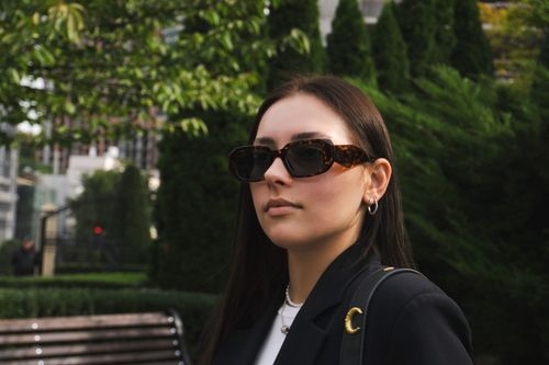 Free Fashionable young woman in sunglasses posing outdoors in a green urban setting. Stock Photo