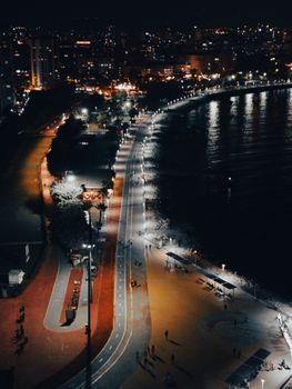 Stunning aerial view of a vibrant city shoreline illuminated at night with reflections on the sea.