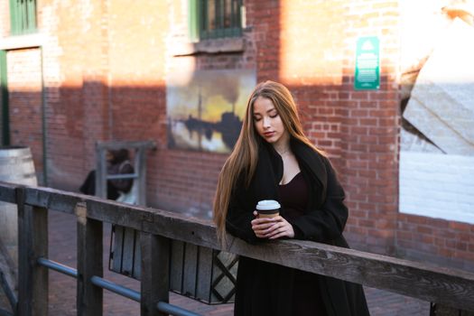 Young woman standing in an urban setting holding coffee, showcasing fashion.