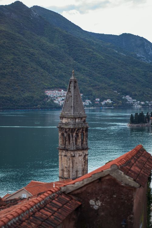 Free Vertical shot of a historic church tower by the bay in Montenegro, surrounded by mountains and sea. Stock Photo