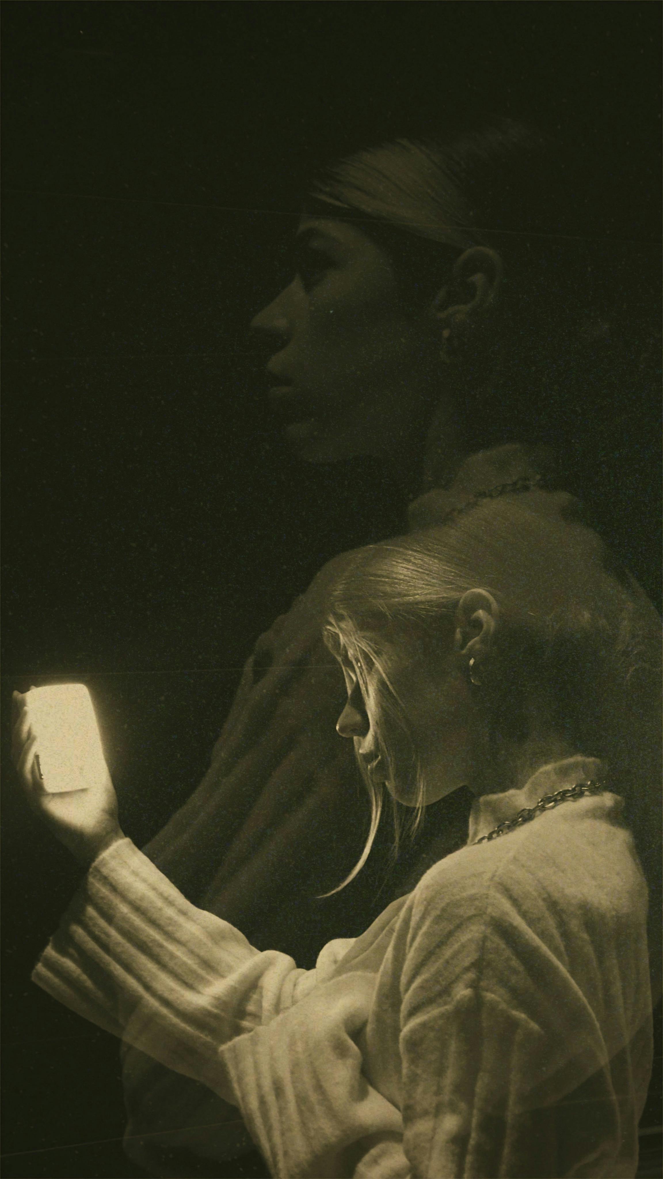 Artistic black and white double exposure of a woman illuminated by phone light, creating a dramatic effect.