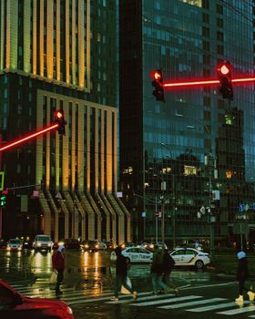 A vibrant city scene at night with pedestrians crossing under red traffic lights.