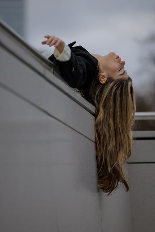 Free Woman leaning back on urban wall in Berlin, showcasing long hair and contemplative expression. Stock Photo