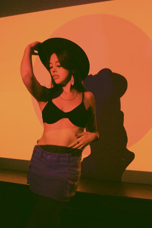 Young Woman Posing in Fedora Hat, Black Bra, and Denim Mini Skirt